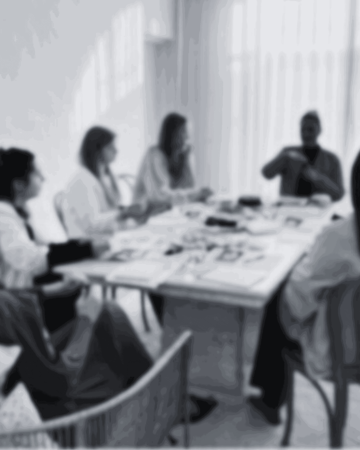 Group of people sitting around a table having a discussion in a well-lit room. Papers are spread on the table.