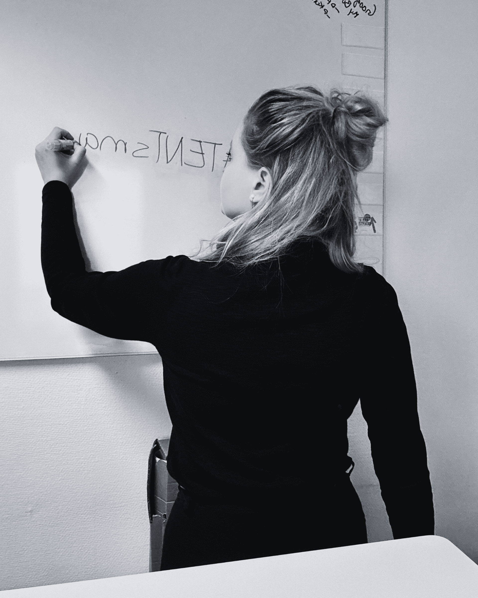 A person with long hair diligently maps out the intricacies of ip strategy, thoughtfully writing "#tenism" on a whiteboard with a black marker.